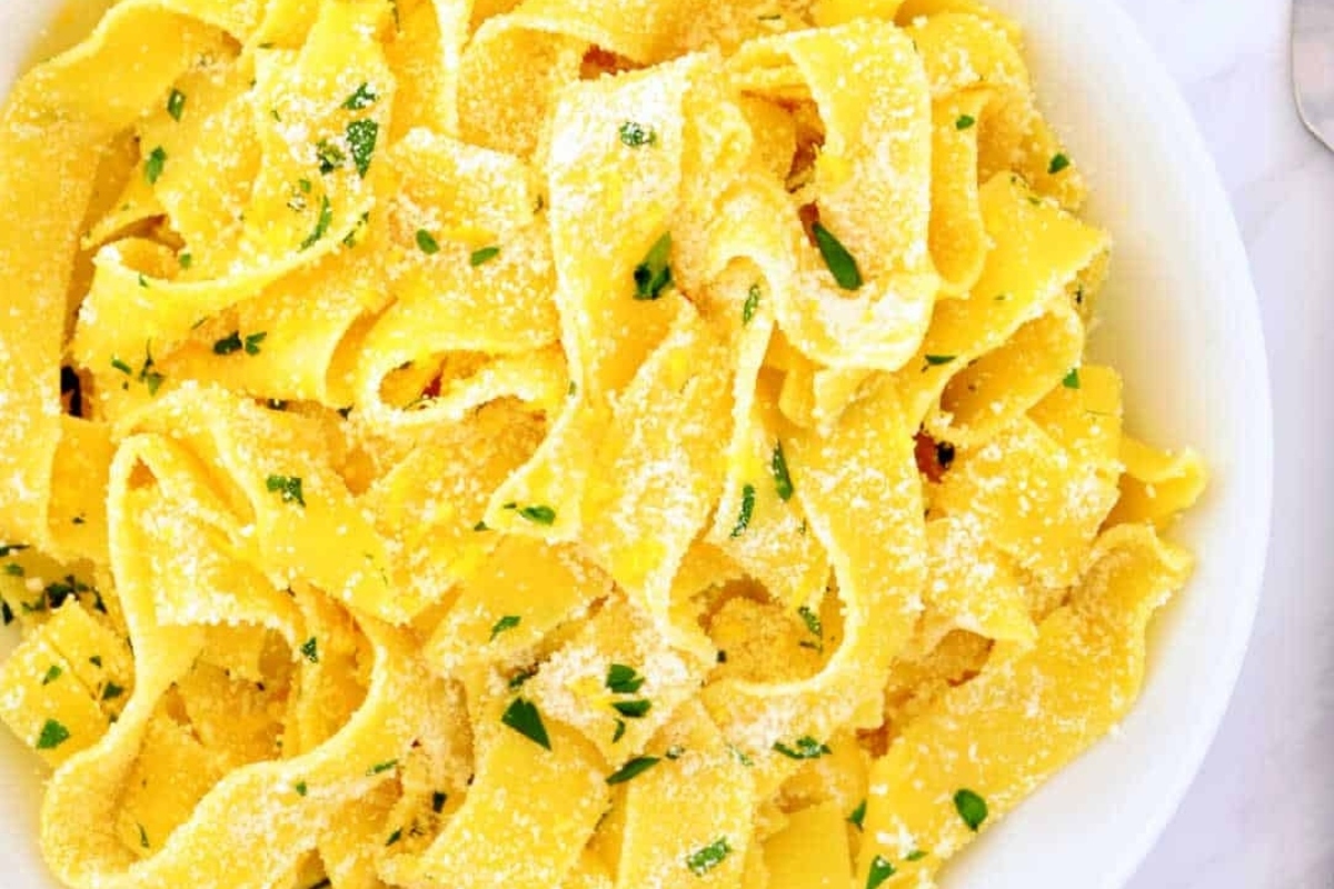 Fettuccine pasta with parmesan cheese and parsley in a white bowl.