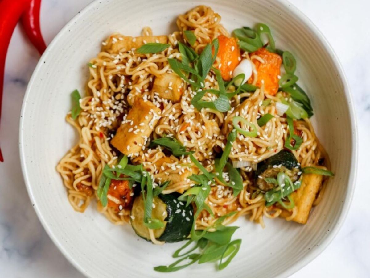Bowl of noodle stir fry with chili, carrot and green onions.