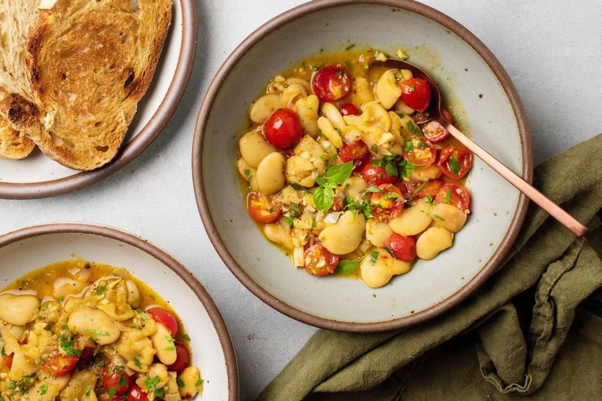 Two bowls of white beans with tomatoes and bread.
