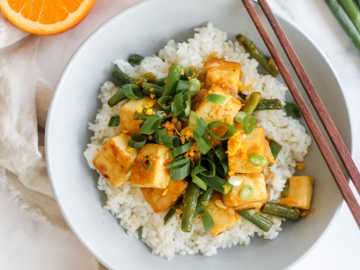 Bowl of orange tofu on rice with chopsticks.