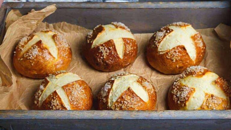 Freshly baked pretzel buns with salt crystals on top, arranged on a baking sheet with parchment paper.