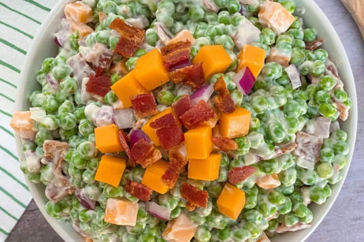 A bowl of pea salad with cubed cheese and bacon pieces on top.