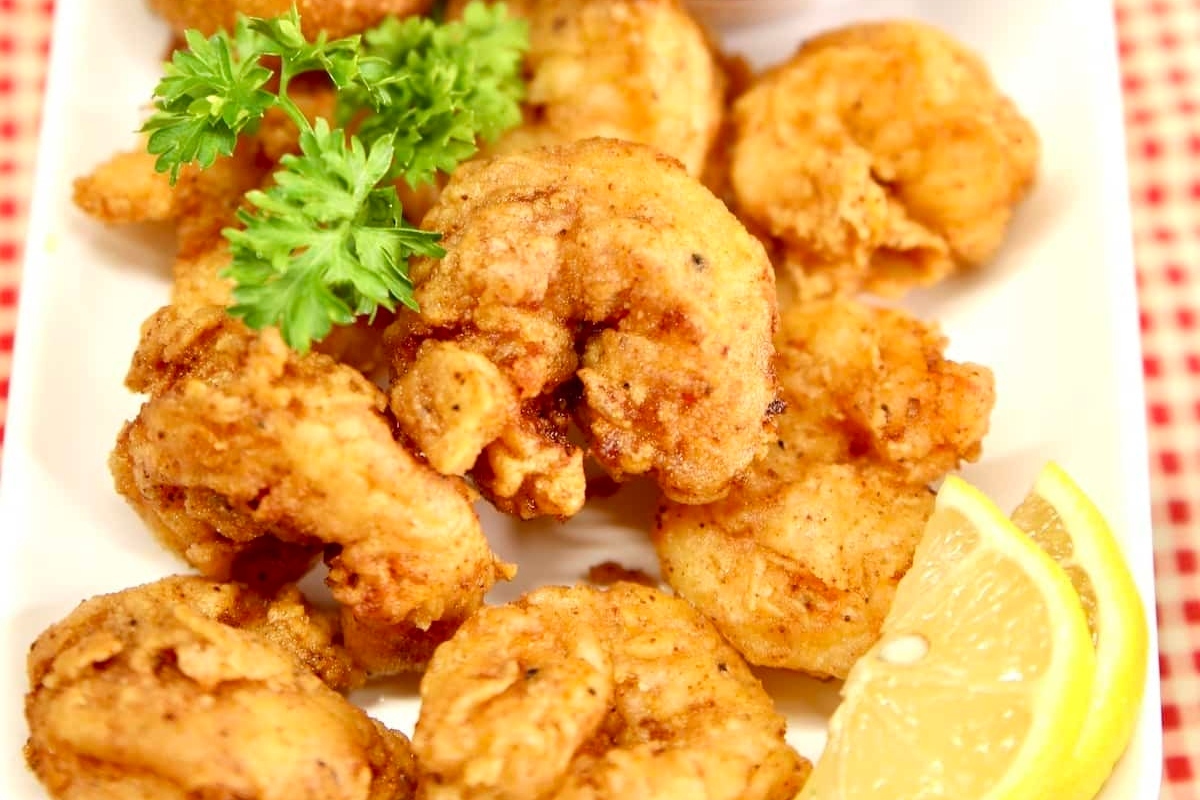 Fried shrimp on a white plate with lemon wedges.