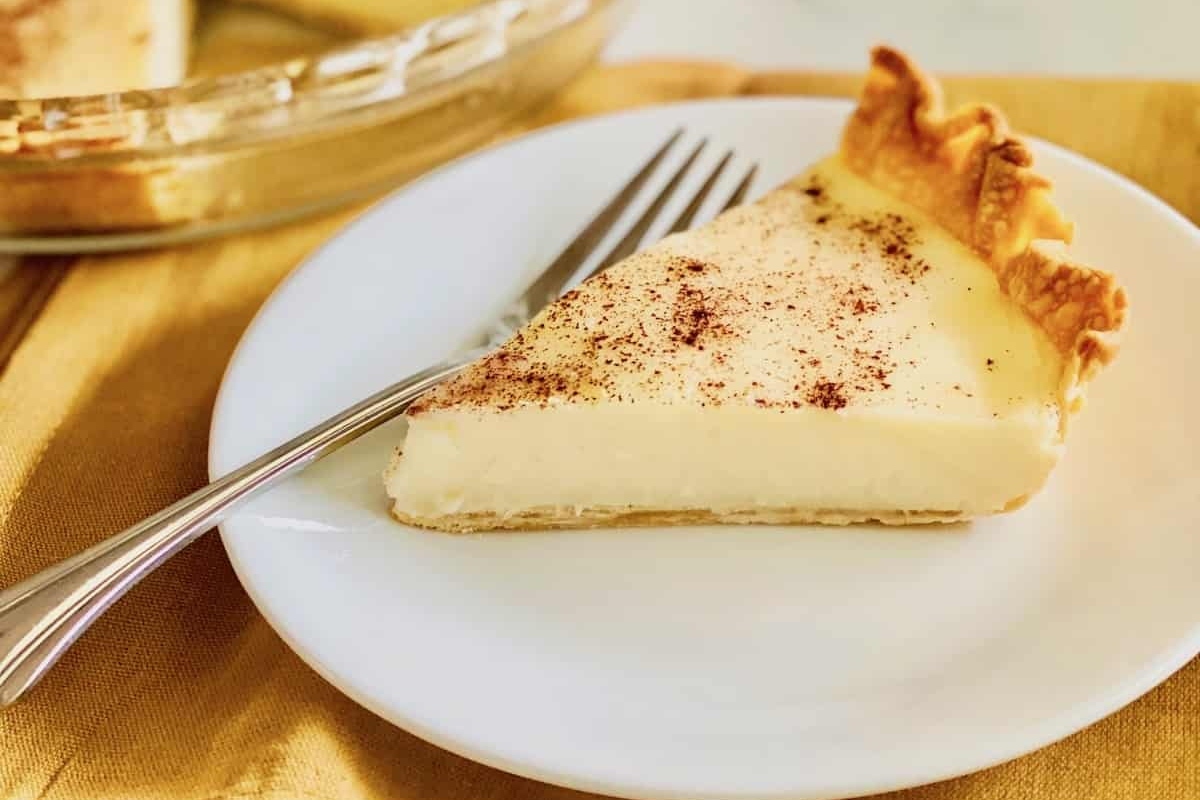 A slice of custard pie with a sprinkle of cinnamon on a white plate with a fork.