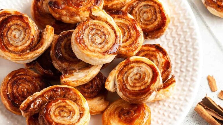 Cinnamon rolls on a plate with cinnamon sticks.