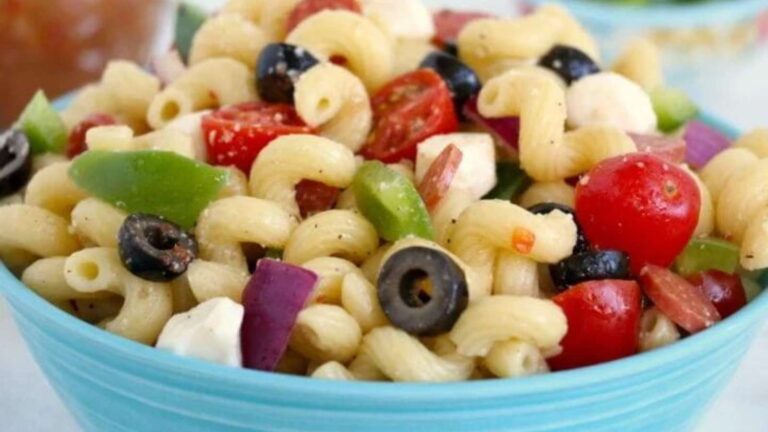 A bowl of pasta salad with cherry tomatoes, olives, onions, and green peppers.