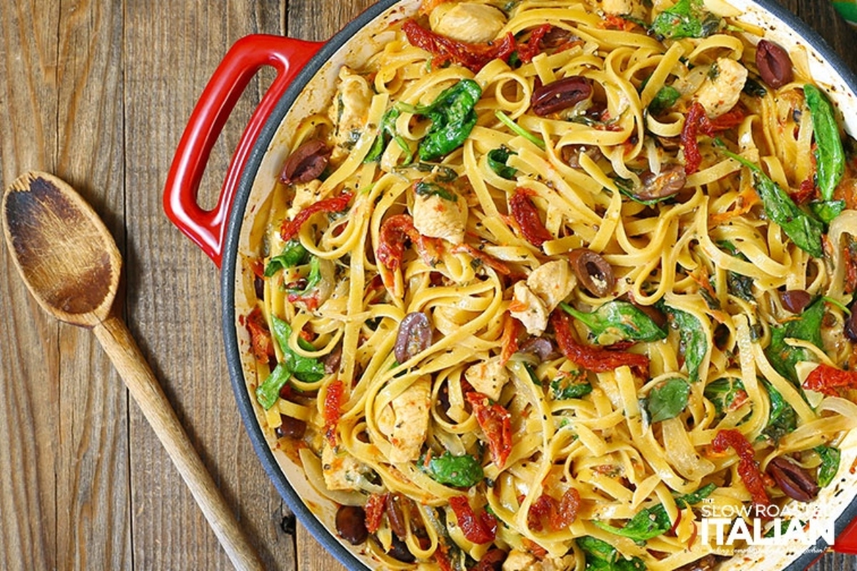 A pan of chicken and vegetable pasta on a wooden table.