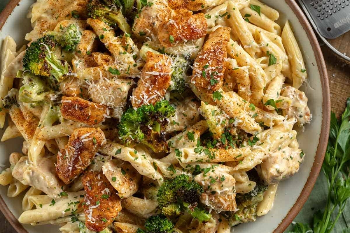 Creamy pasta with grilled chicken and broccoli, sprinkled with grated cheese.