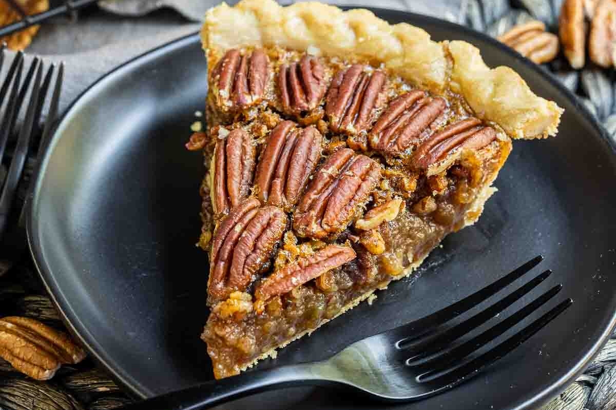 A slice of pecan pie on a black plate.