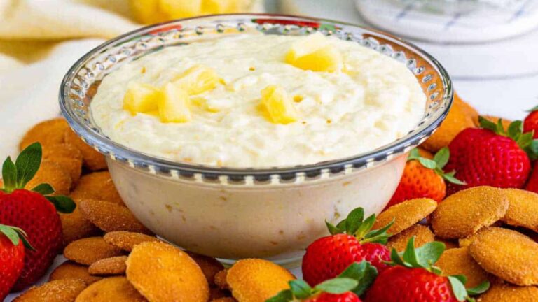 Bowl of pineapple dip garnished with pineapple pieces served with strawberries and vanilla wafers.