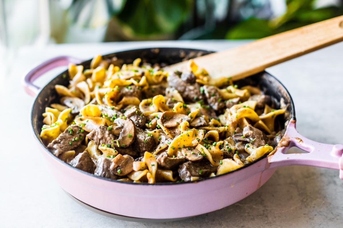 Beef stroganoff in a pink pan with a wooden spoon.