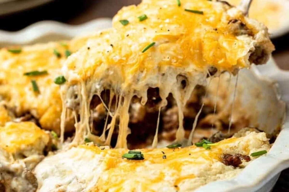 A dish of cheesy, baked cheeseburger pie being served with melted cheese stretching from the pan.
