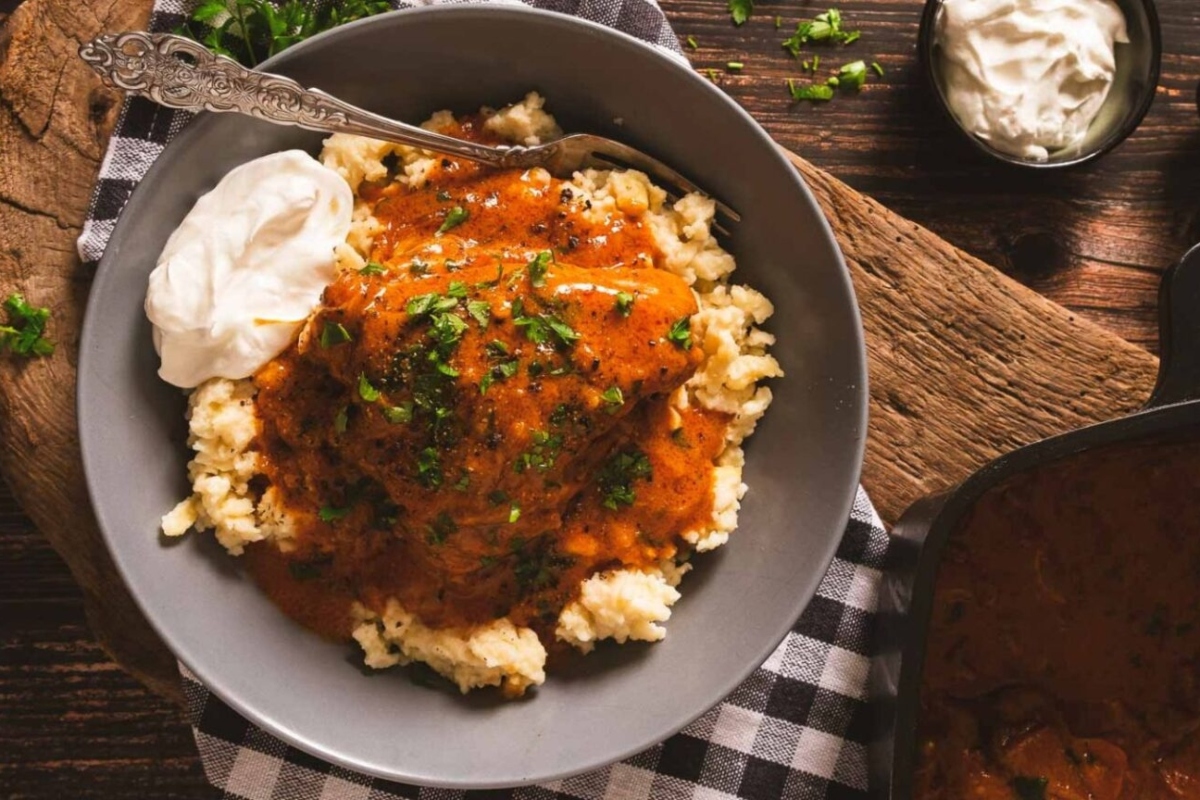 A bowl of stew with rice and sour cream.