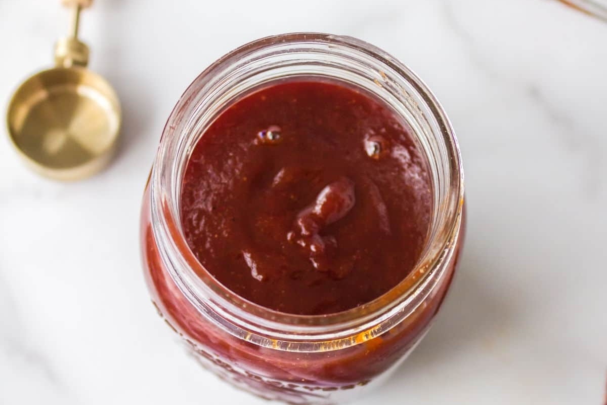 Open jar of BBQ sauce with a golden spoon nearby.