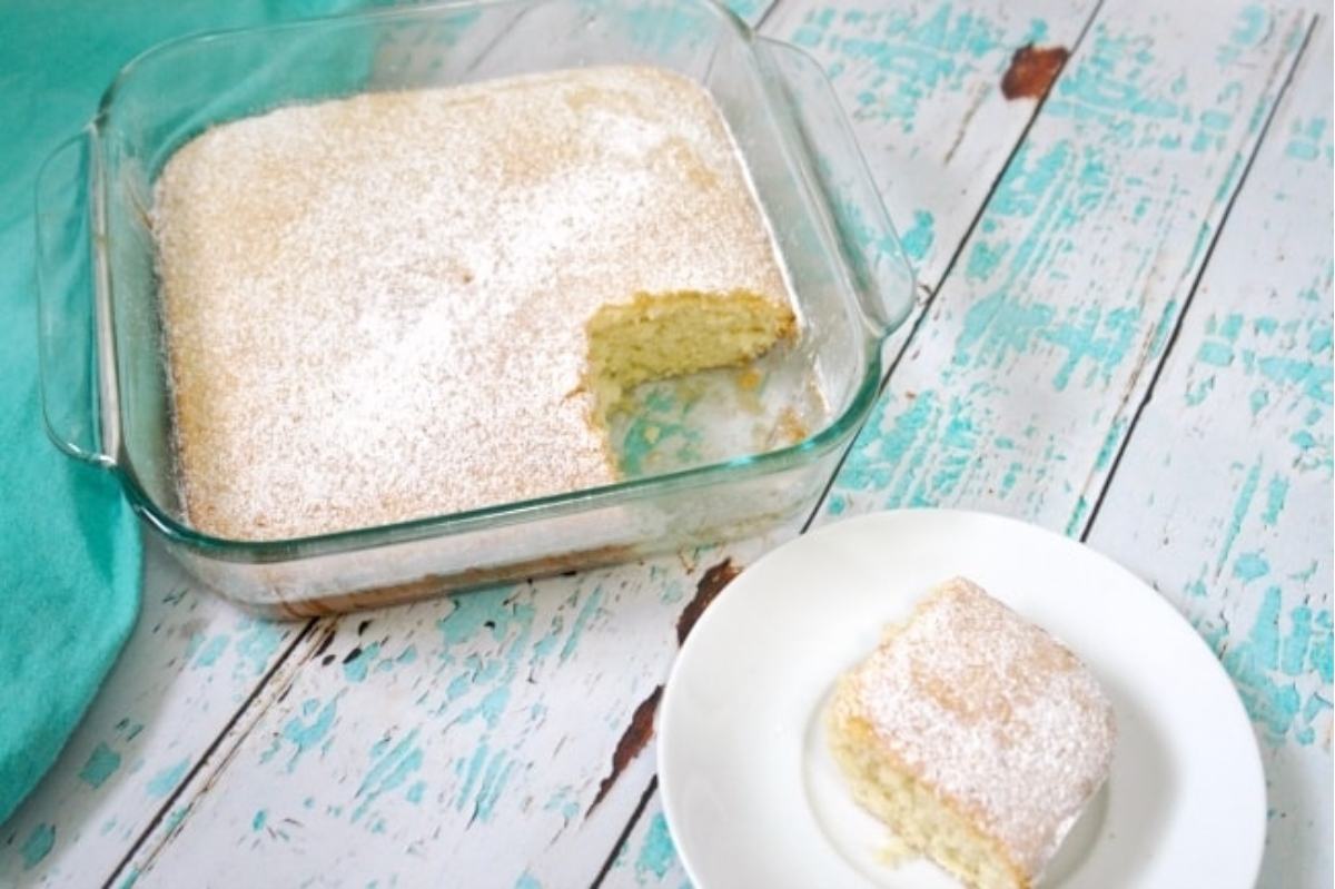 Freshly baked cake dusted with powdered sugar, with one piece served on a plate.