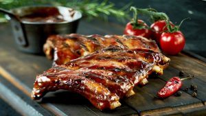 Spicy hot grilled spare ribs from a summer BBQ served with a hot chili pepper and fresh tomatoes on an old vintage wooden cutting board