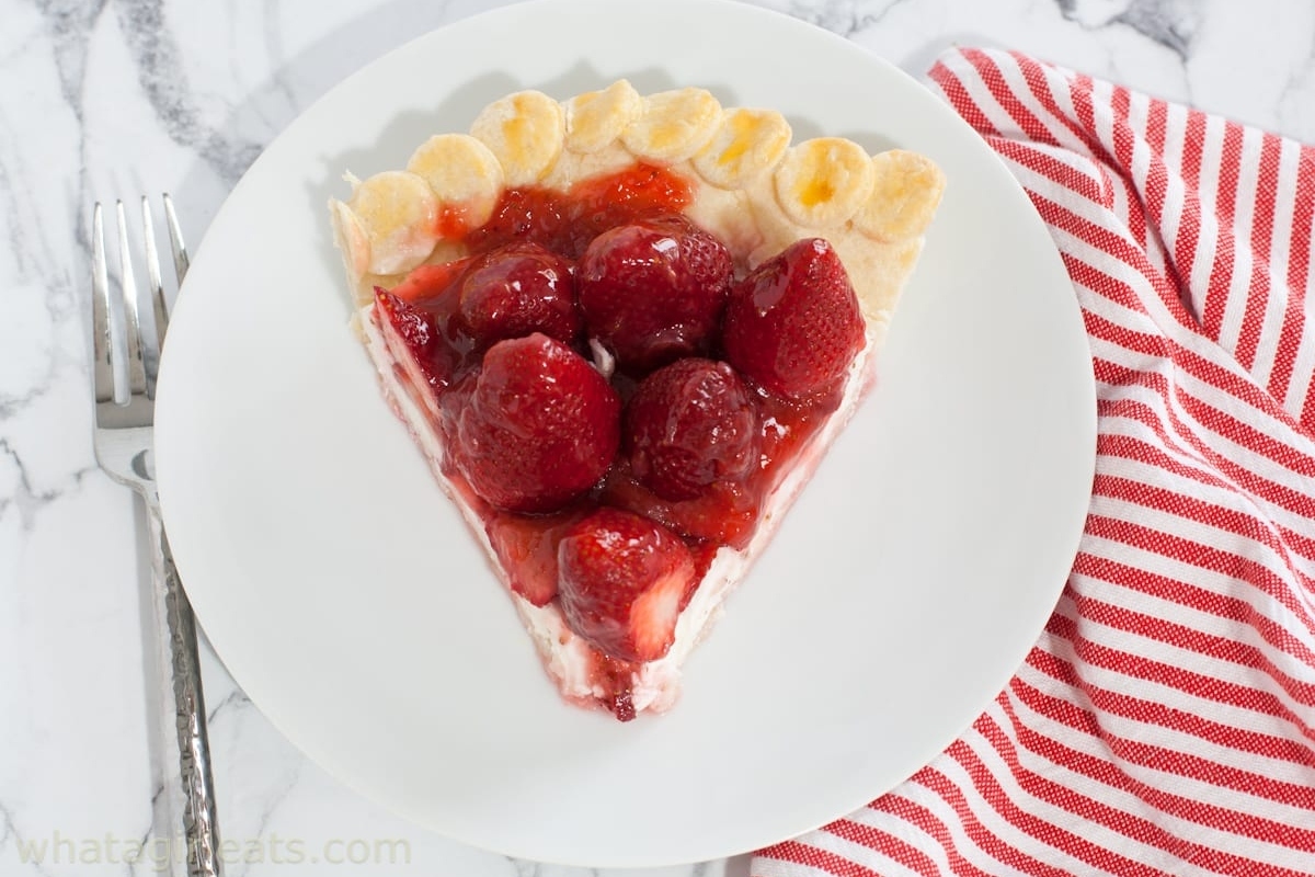 A slice of strawberry pie on a white plate with a red and white striped napkin on the side.