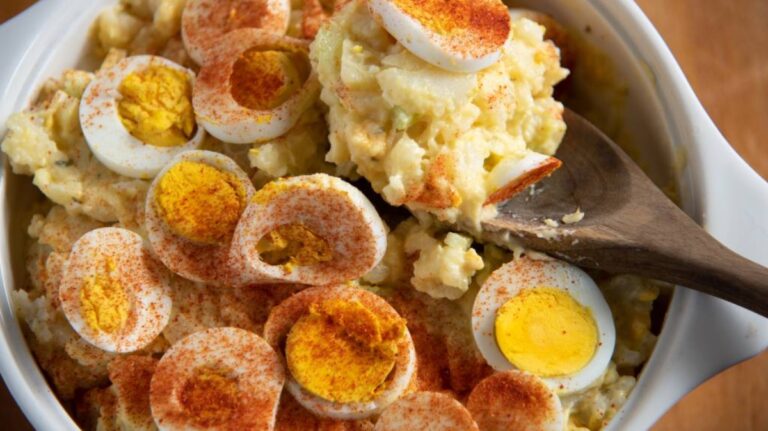 A bowl of potato salad topped with sliced hard-boiled eggs and paprika.