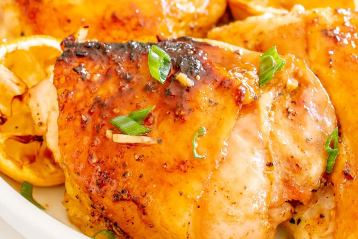 23 Finger-Lickin' Good Chicken Thigh Recipes That Are Simply Irresistible 17 Close-up of a plate with cooked, glazed chicken breasts garnished with green onions and lemon slices, perfect for any lemon recipes collection.