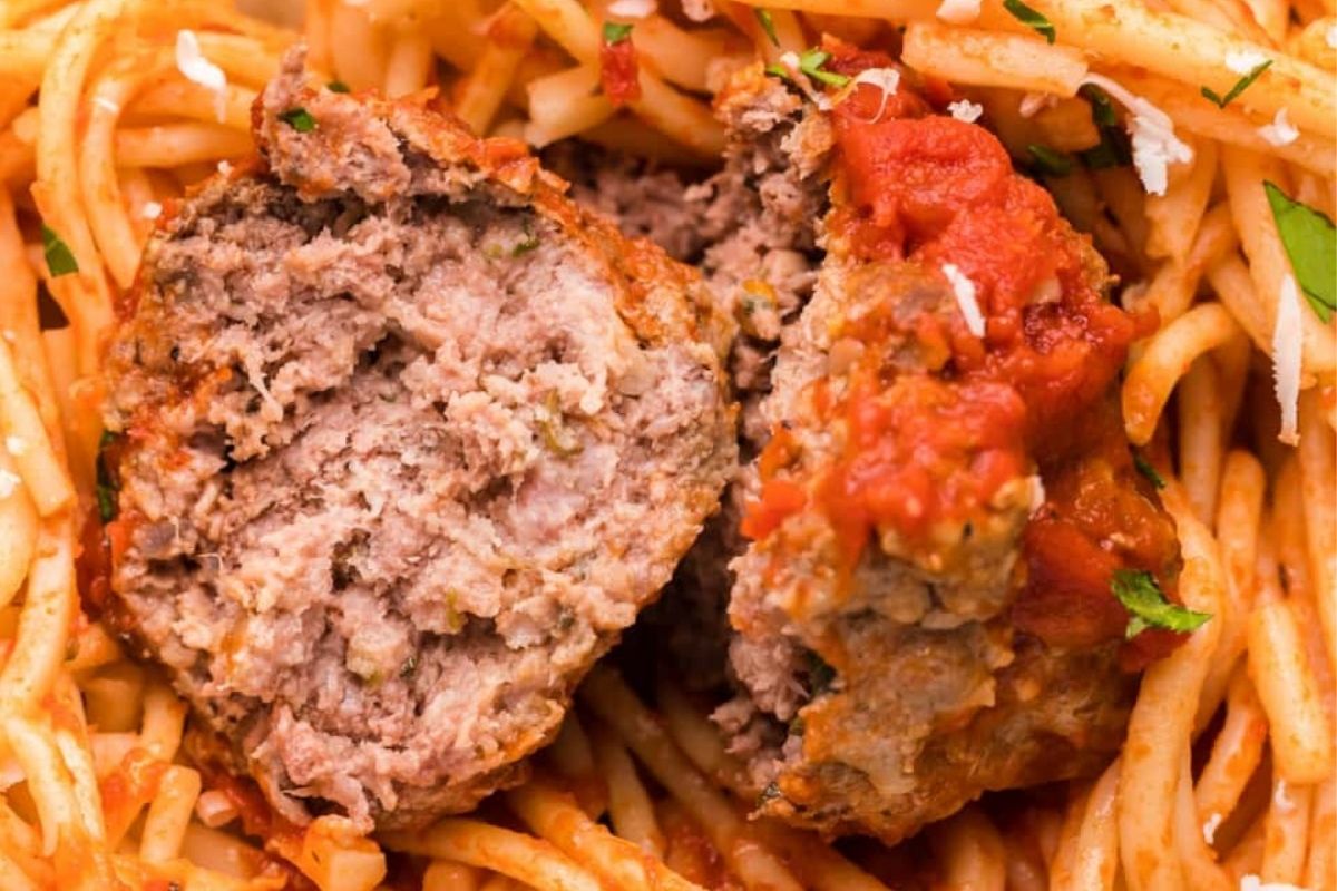 A close-up view of recipes featuring noodles: spaghetti with tomato sauce and a halved meatball, garnished with grated cheese and herbs.