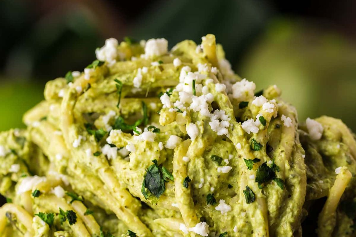 A close-up of recipes featuring noodles with pesto sauce and crumbled cheese topping.