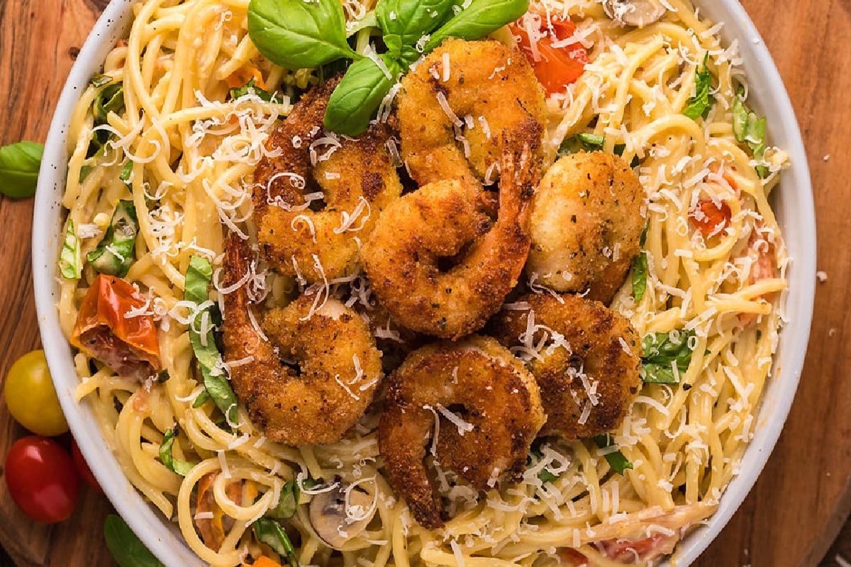 A bowl of spaghetti noodles garnished with breaded shrimp, grated cheese, fresh basil leaves, cherry tomatoes, and green herbs showcases the best of Italian cuisine.