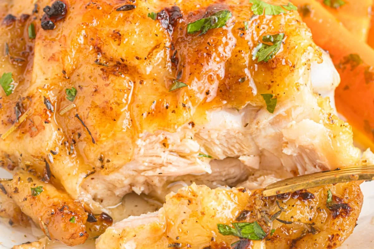 23 Finger-Lickin' Good Chicken Thigh Recipes That Are Simply Irresistible 19 Close-up of a golden-brown, roasted chicken breast garnished with herbs and served with a side of sliced carrots.