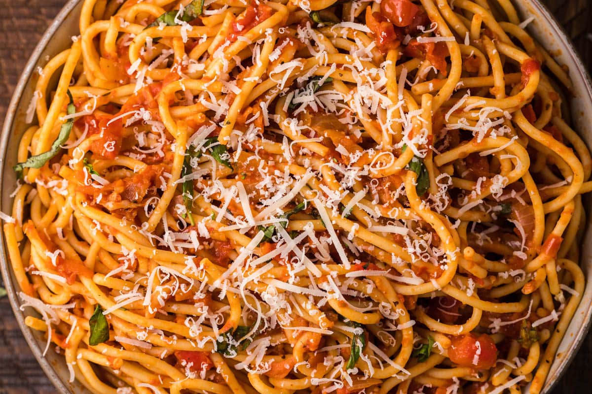 A plate of Pasta Napoletana topped with tomato sauce, fresh basil, and grated cheese.