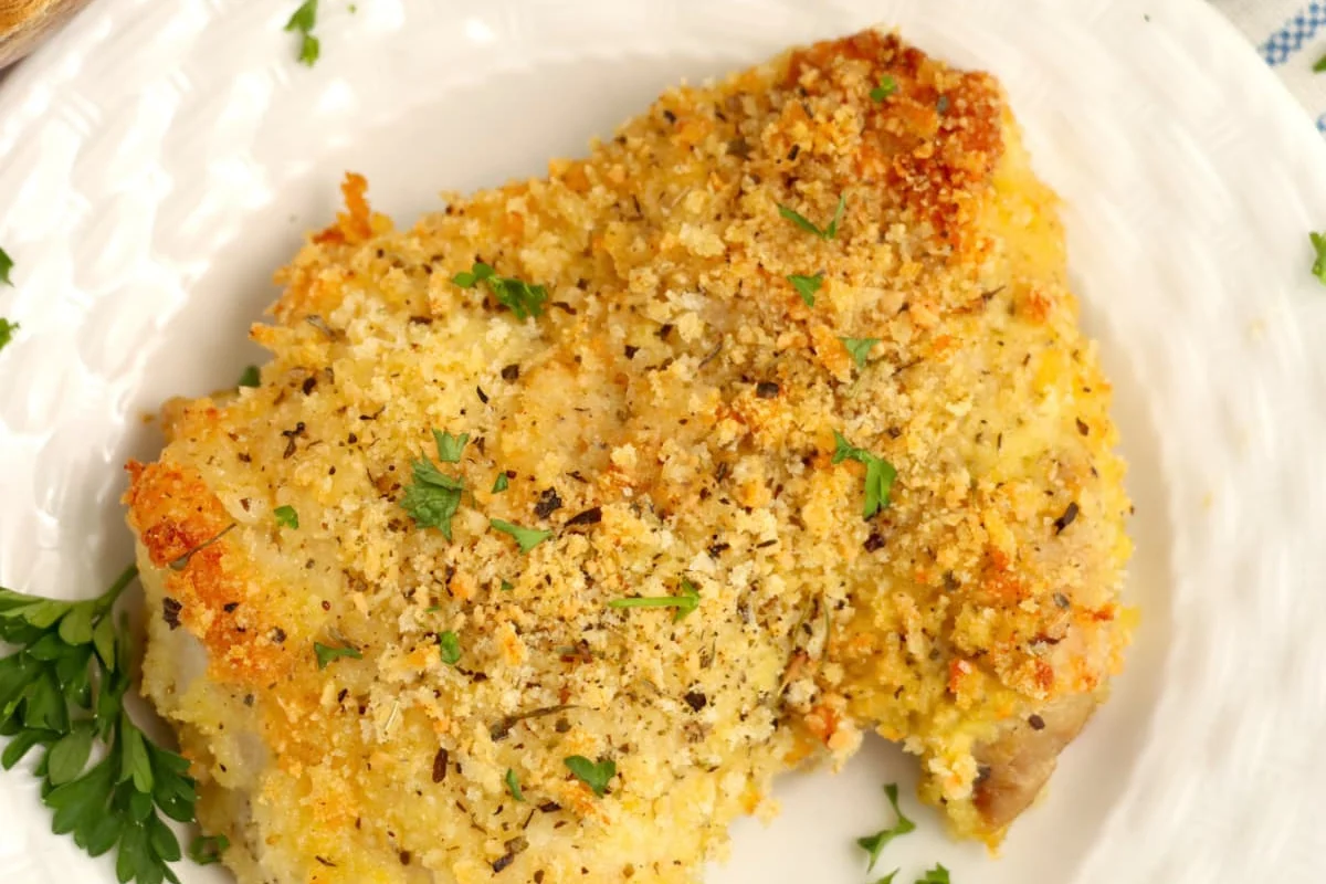 23 Finger-Lickin' Good Chicken Thigh Recipes That Are Simply Irresistible 18 A piece of breaded and seasoned chicken or fish is served on a white plate, garnished with chopped parsley. This dish is one of those irresistible chicken recipes that everyone will love.