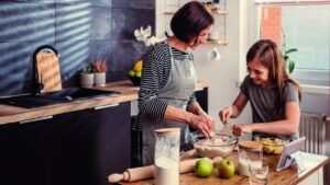 Mother and daughter making together dough for apple pie at kitchen